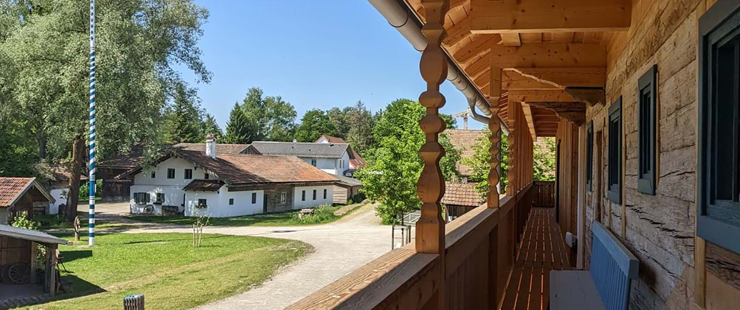 Traditionelle Gebäude mit Satteldächern und Maibaum in einem Freilichtmuseum, Blick vom Holzbalkon aus.