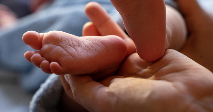 Eine erwachsene Hand hält sanft einen kleinen Babyfuß.